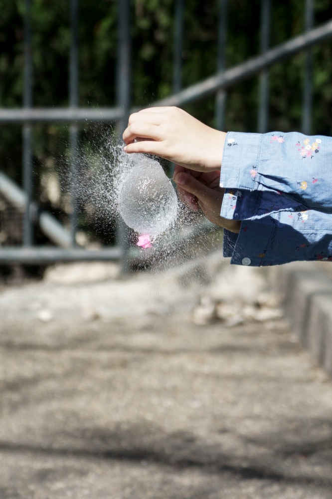 Girl&rsquo;s hands blowing up a water balloon with a needle outdoors. Girl&rsquo;s hands blowing up a water balloon with a needle
