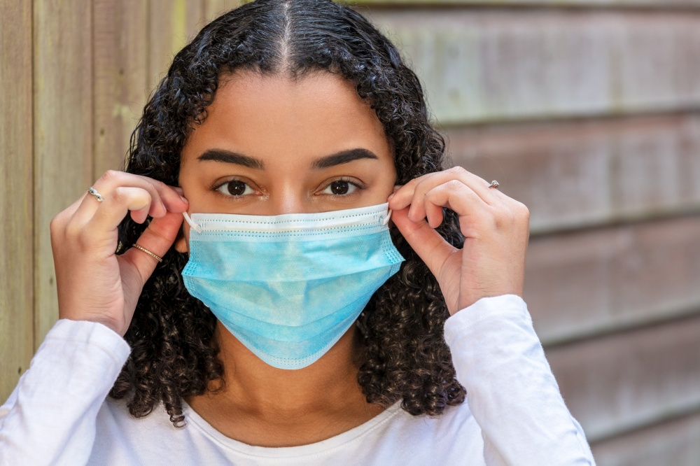 Mixed race teenager teen girl young woman wearing adjusting and fitting a face mask during the Coronavirus COVID-19 pandemic