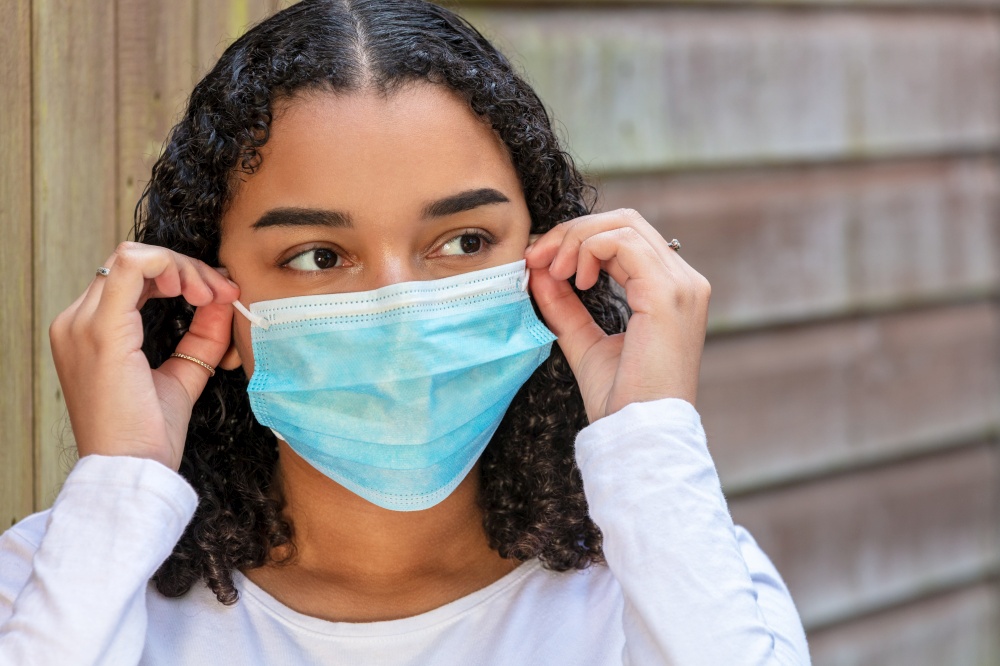 Mixed race teenager teen girl young woman wearing fitting and adjusting a face mask during the Coronavirus COVID-19 pandemic