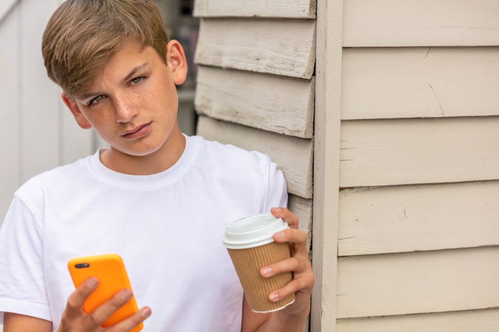 Boy teenager teen male child outside using his mobile cell phone and drinking takeout tea or coffee