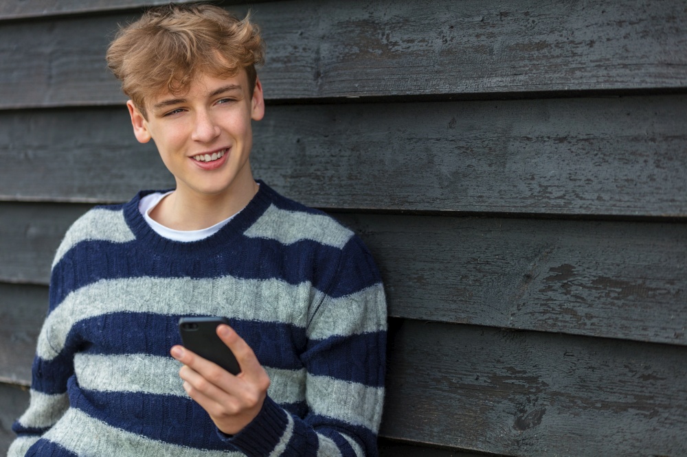 Smiling Happy male boy teenager outside leaning wall using his mobile cell phone for social media or video call