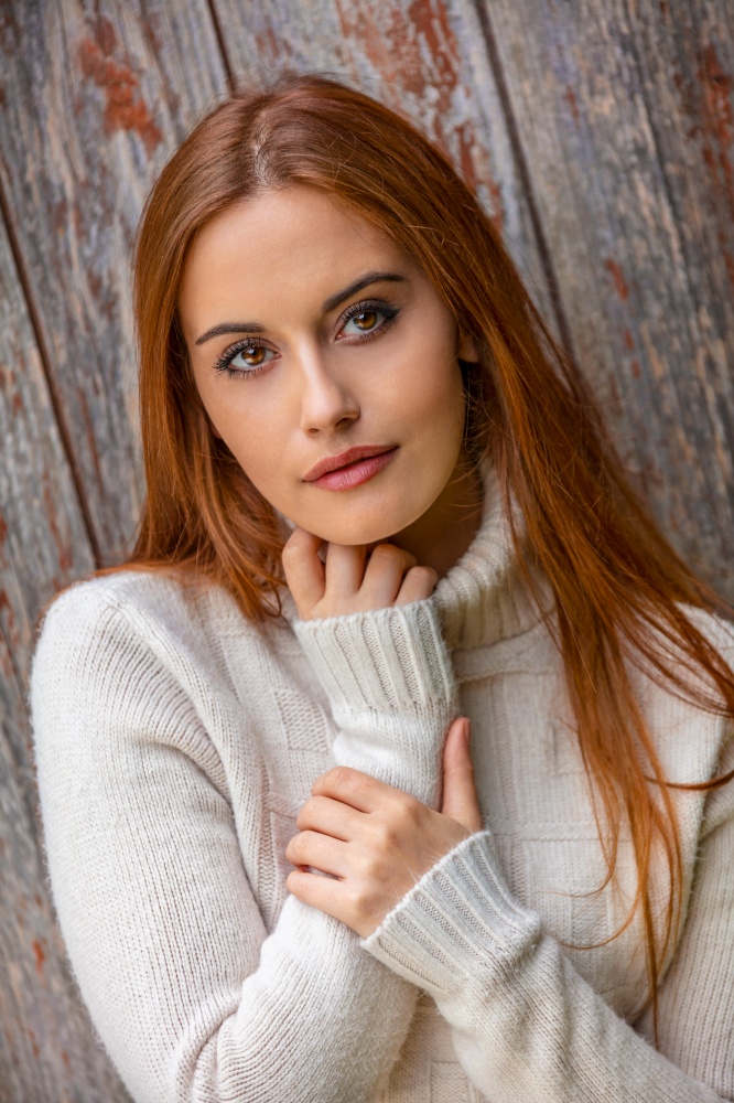 Outdoor portrait of beautiful thoughtful sad or depressed girl or young woman with red hair wearing a white jumper