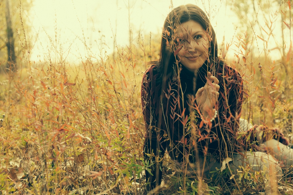 Girl is sitting in tall autumnal grass