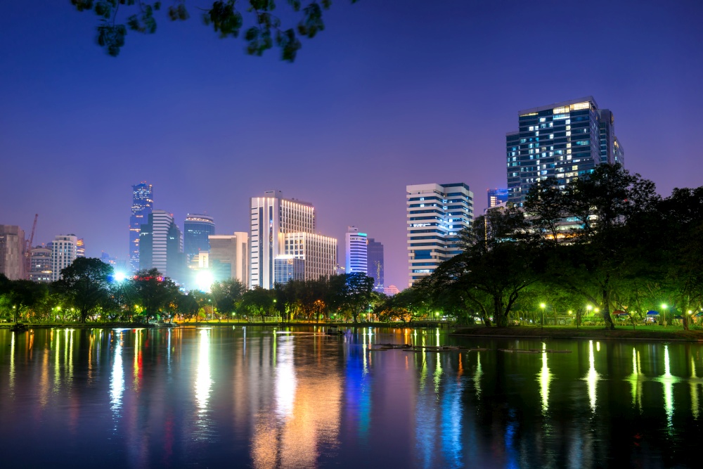 Bangkok city at night - Architecture of capital city. Landscape night view of illuminated skyscrapers buildings on skyline and their reflection in lake water in Lumphini park in Bangkok, Thailand