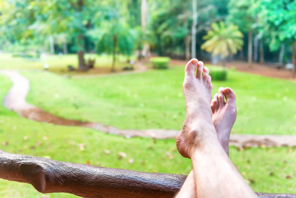 Bare feet of resting man on green lawn background. Erawan National park, Thailand. Relax lifestyle concept