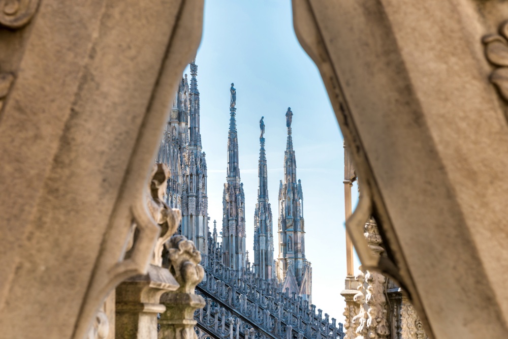 View to spires and statues on roof of Duomo through ornate marble fencing. Milan, Italy