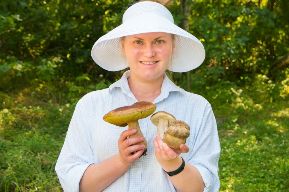 Pretty young woman in forest with big Boletus Edulis or Penny Bun mushrooms in hands