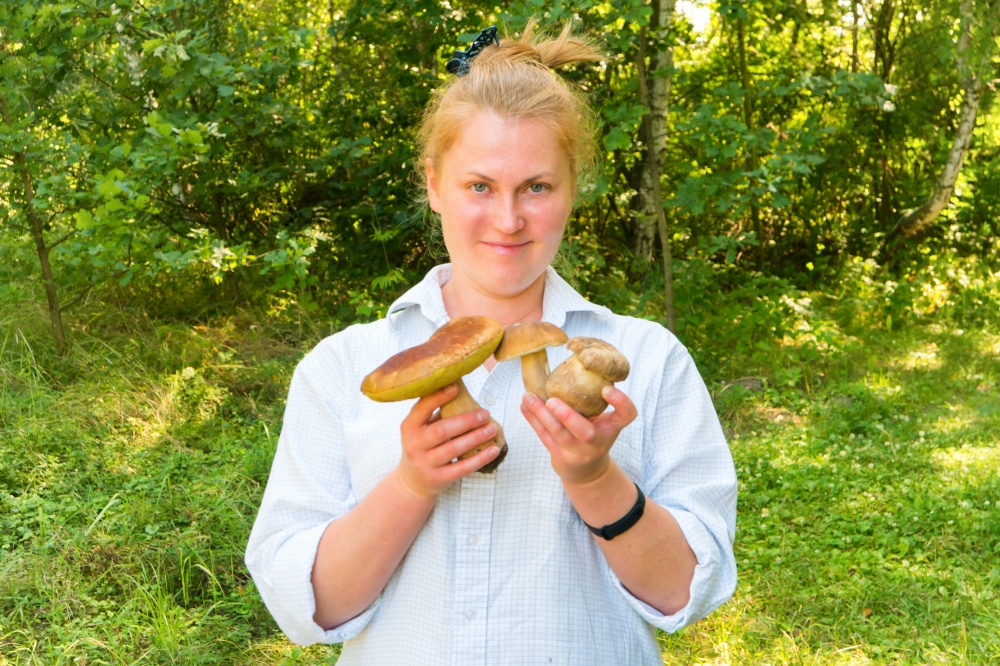 Pretty young woman in forest with big Boletus Edulis or Penny Bun mushrooms in hands