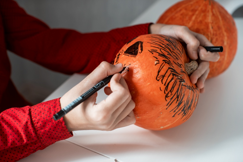 Happy teen boy in costume preparing for the Halloween celebration drawing a pumpkin. Halloween carnival or masquerade concept. Halloween carnival or masquerade concept