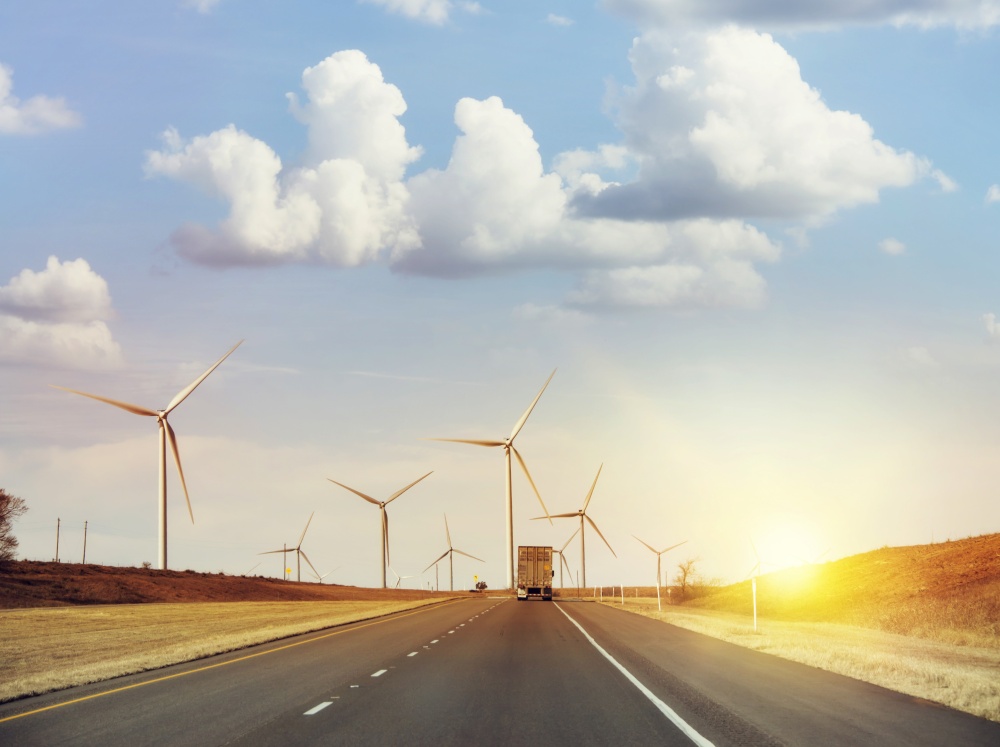 Traffic moves along an interstate highway with wind turbines at sunset