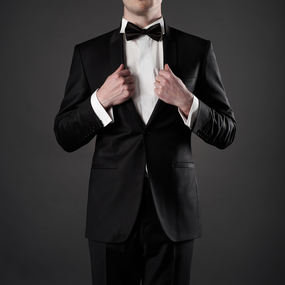 Photo of stylish man in elegant black suit with tie. Fashionable young model pose in photography studio. Luxury evening smoking with white shirt.