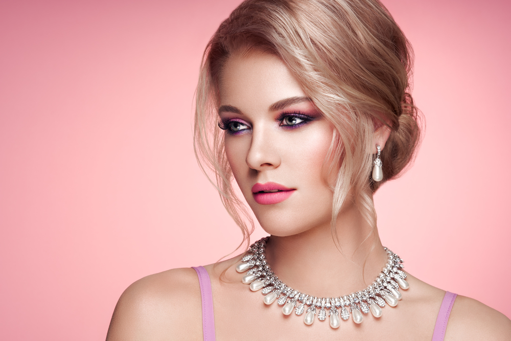 Portrait Beautiful Blonde Woman with Jewelry. Elegant Hairstyle.  Beauty and Fashion Accessories. Perfect Make-Up. Pink Background