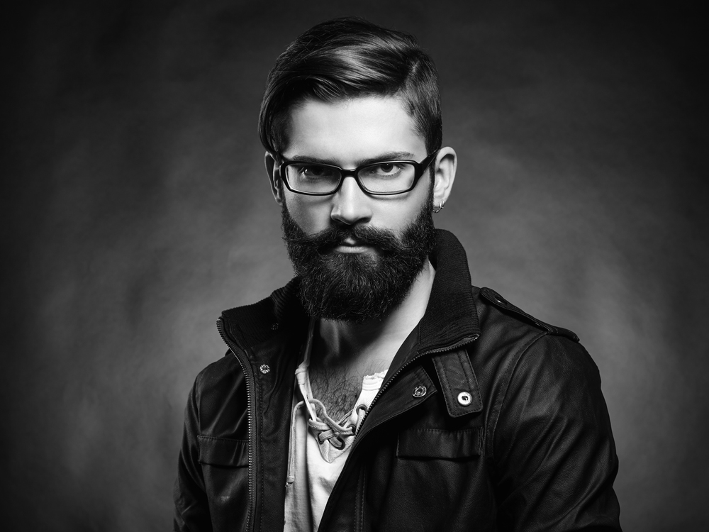 Portrait of handsome man with beard and mustache. Close-up image of serious brutal bearded man on dark background. Man with glasses. Black and white photography