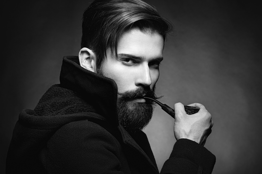 Brutal man with a beard and mustache Smoking a pipe. Close-up image of serious bearded man on dark background. Black and white photography