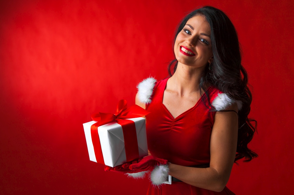 Smiling cute girl in red christmas outfit holding gift box. Girl with christmas gift box