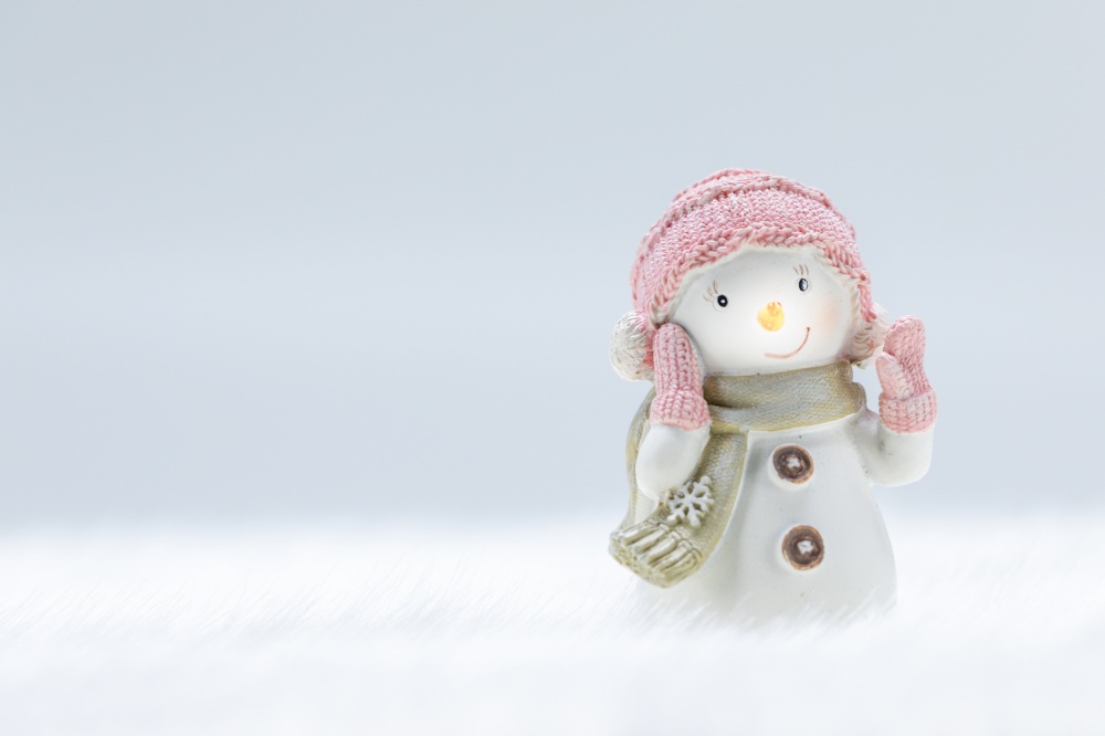 Female Snowman toy on frozen snow light winter background with copy space. Snowman toy on winter background
