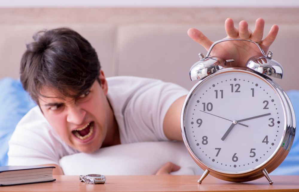 Man in bed frustrated suffering from insomnia with an alarm clock. Man in bed frustrated suffering from insomnia with an alarm cloc