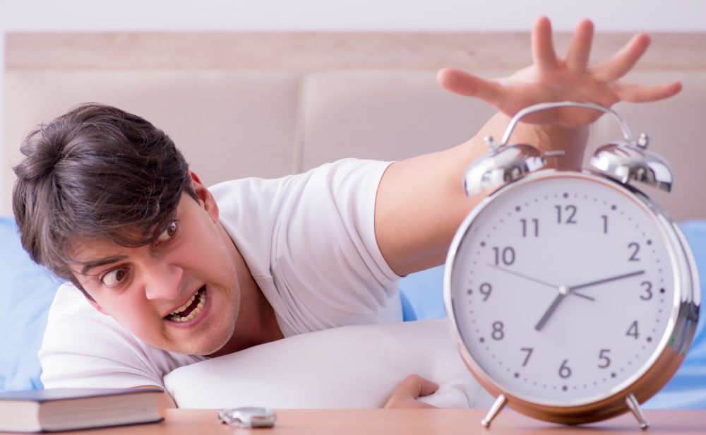 Man in bed frustrated suffering from insomnia with an alarm clock. Man in bed frustrated suffering from insomnia with an alarm cloc