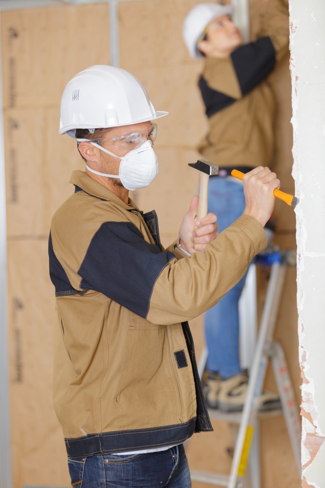 builders working indoors man in foreground using hammer and chisel