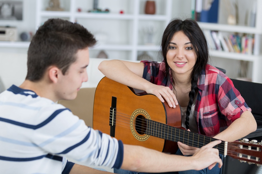 young man teaches his girlfriend to play the guitar indoors