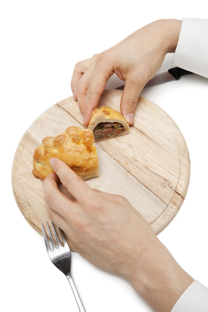 Hands holding Cornish pastry cut into two pieces on wooden plate over white background