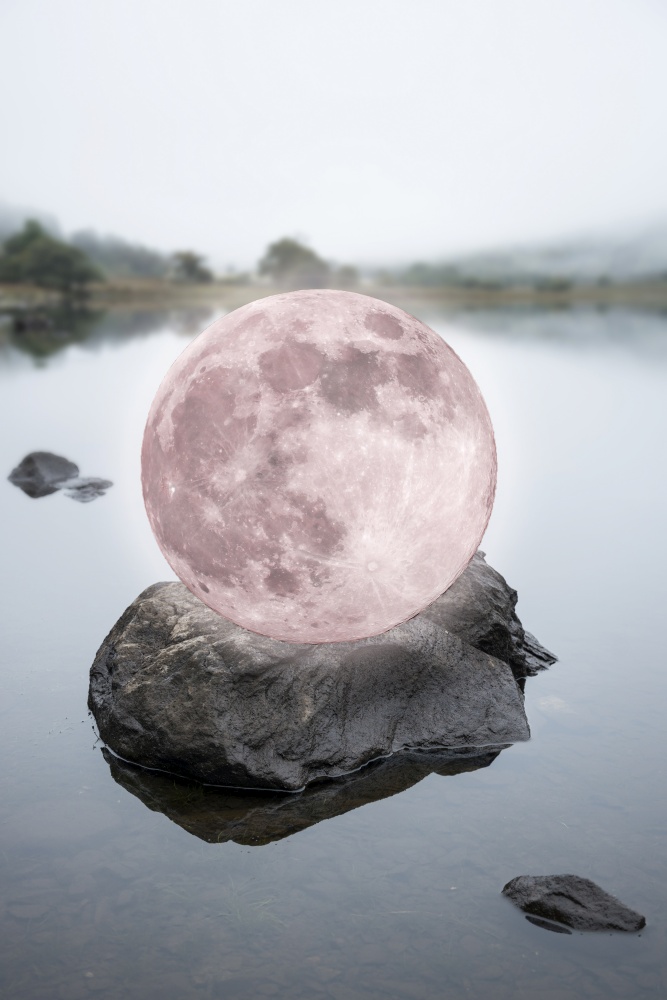 Digital composte of surreal pink or red Super Moon sitting on top of a rock on a calm lake surface giing a fantasy type or syle look to the image