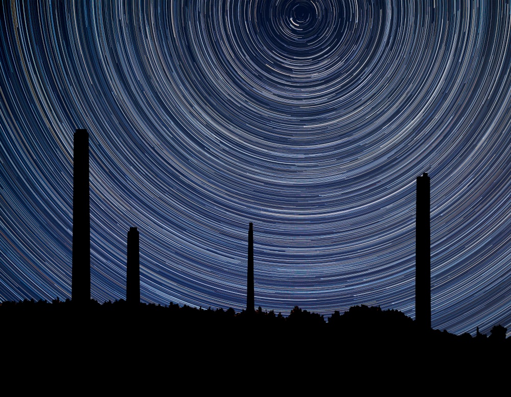 Digital composite image of star trails around Polaris with industrial chimney stacks landscape