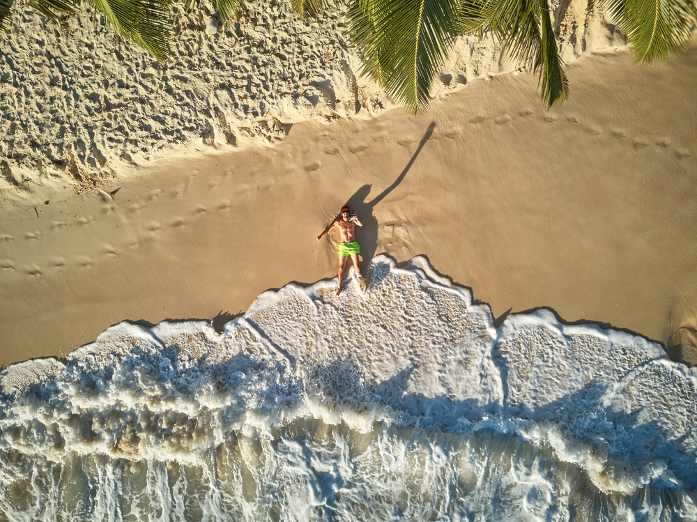 Man lying down on beach aerial top view drone shot at Seychelles, Mahe