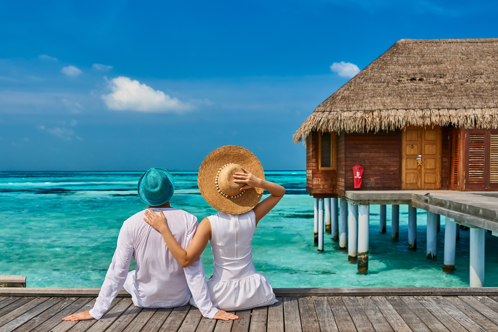 Couple in white on a tropical beach jetty near water villa at Maldives