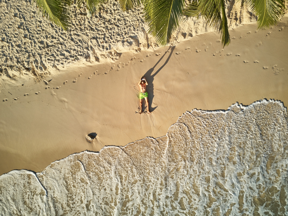 Man lying down on beach aerial top view drone shot at Seychelles, Mahe
