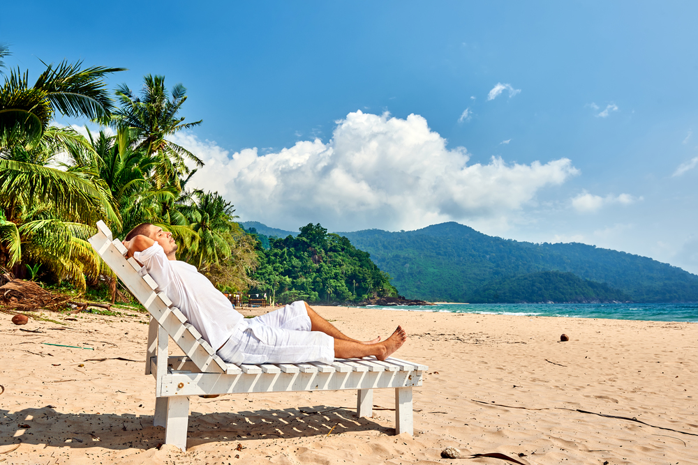 Man in white relaxing in sun bed on a tropical beach at Tioman Island, Malaysia