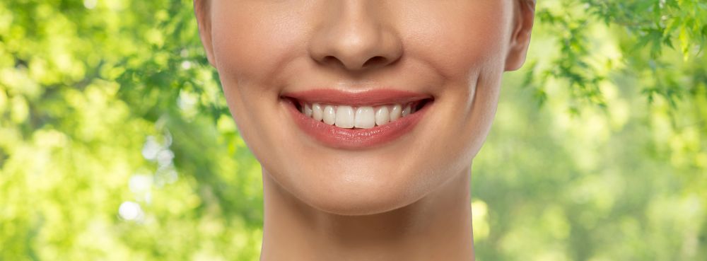 beauty, dental care and teeth whitening concept - close up of beautiful young woman with white smile over green natural background. close up of beautiful young woman with white smile