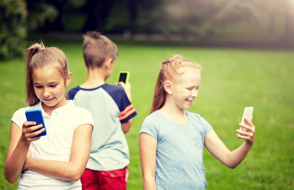 childhood, augmented reality, internet addiction, technology and people concept - group of kids or friends with smartphones playing game in summer park. kids with smartphones playing game in summer park