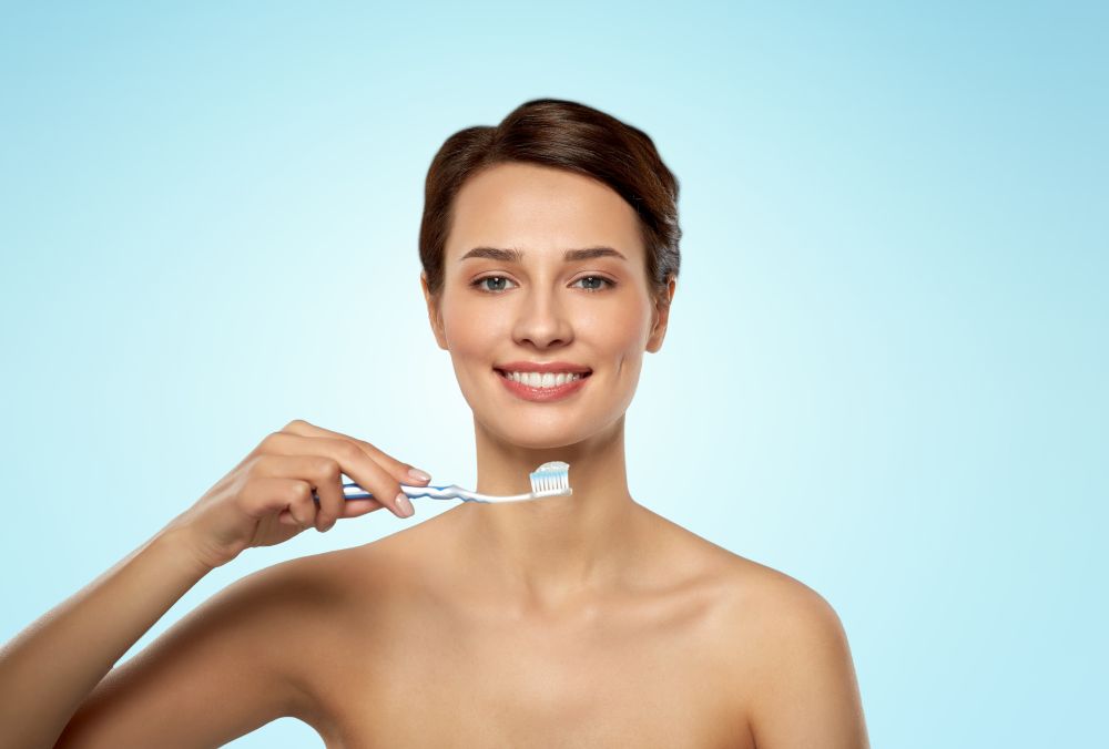 oral hygiene, dental care and health concept - smiling woman with toothpaste on toothbrush cleaning teeth over blue background. smiling woman with toothbrush cleaning teeth
