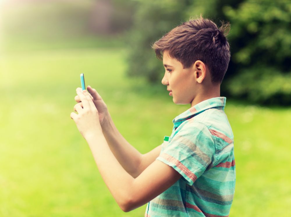 childhood, augmented reality, technology and people concept - boy with smartphone playing game in summer park. boy with smartphone playing game in summer park