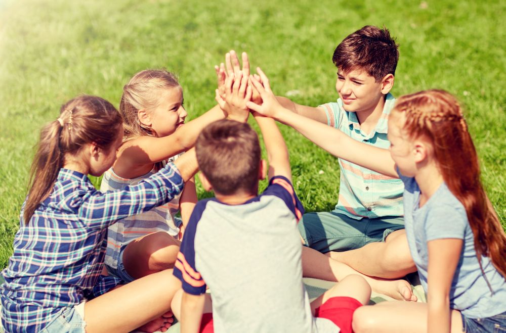 summer holidays, friendship, childhood, leisure and people concept - group of happy pre-teen kids making high five gesture in park. group of happy kids making high five outdoors