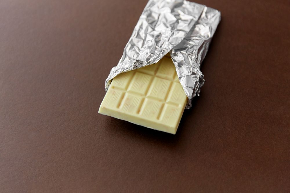 sweets, confectionery and food concept - white chocolate bar in foil wrapper on brown background. white chocolate bar in foil wrapper on brown