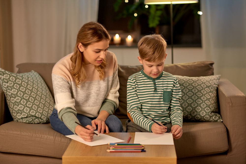 family, leisure and people concept - mother and little son with colored pencils and paper draw at home. mother and son with pencils drawing at home