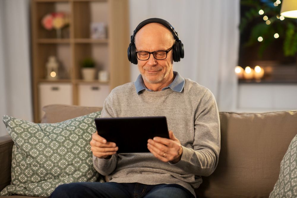 technology, old people and lifestyle concept - happy senior man with tablet pc computer and headphones listening to music at home in evening. senior man with tablet pc and headphones at home
