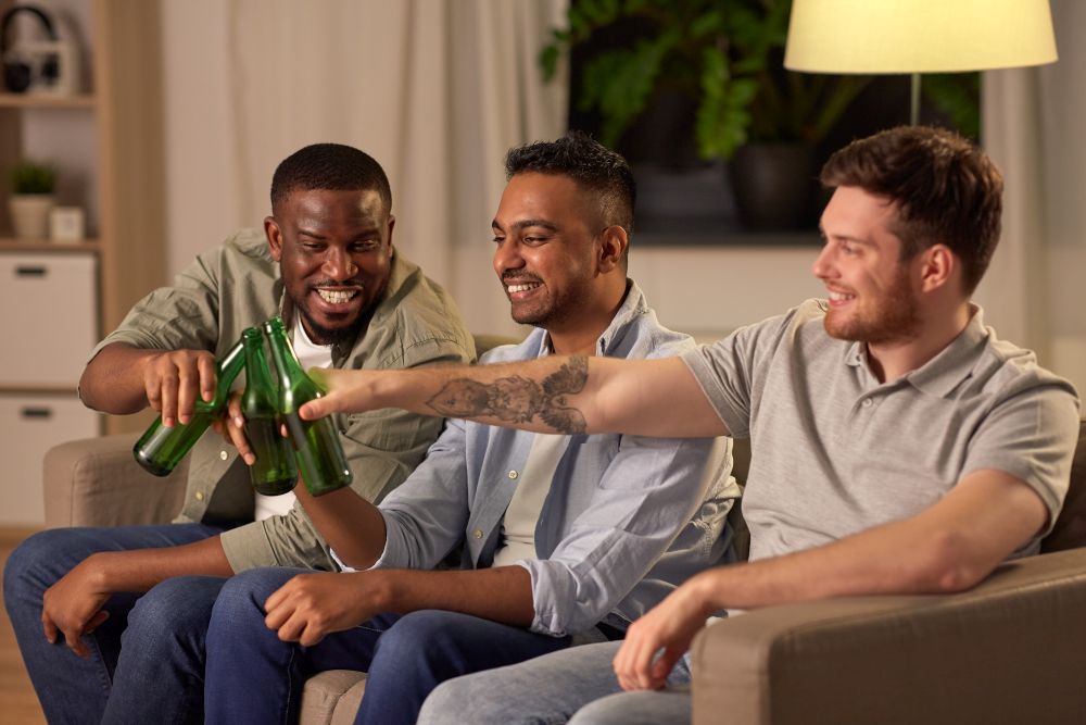 friendship, leisure and people concept - happy male friends drinking beer at home at night. happy male friends drinking beer at home at night