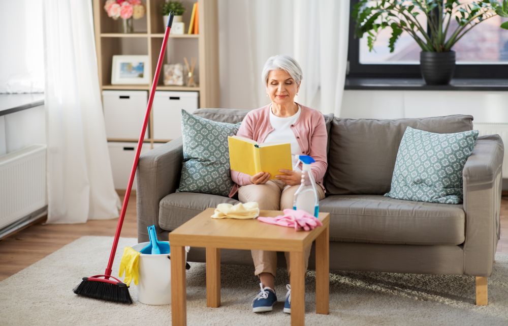 household and people concept - senior woman reading book and resting after home cleaning. senior woman reading book after home cleaning