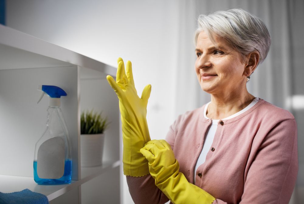 cleaning, housework and housekeeping concept - senior woman putting protective rubber gloves on at home. senior woman putting protective rubber gloves on