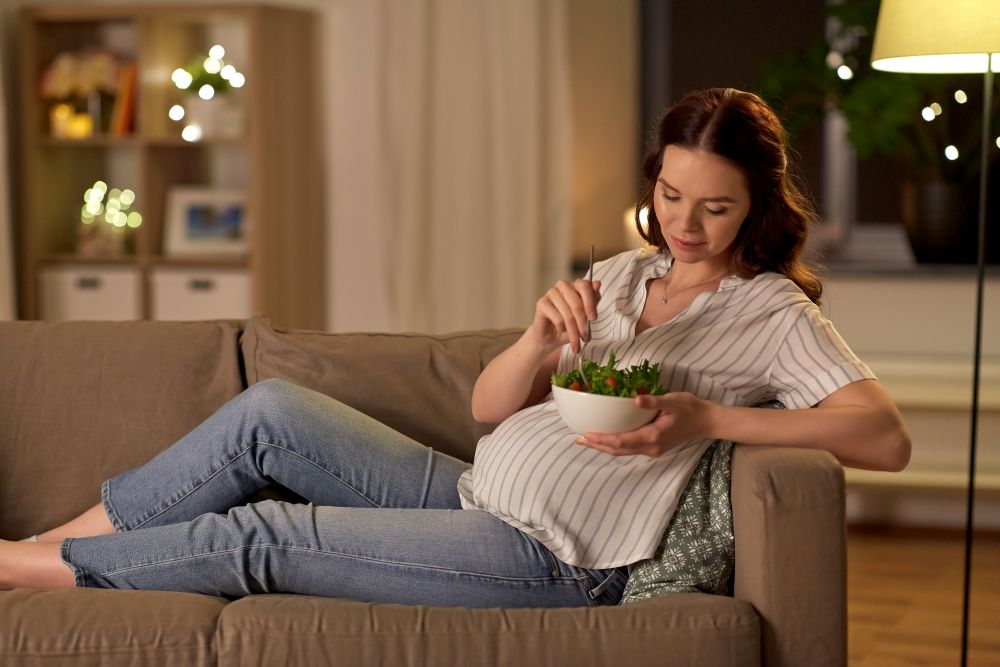 pregnancy, healthy food and people concept - happy smiling pregnant woman eating vegetable salad at home. happy smiling pregnant woman eating salad at home