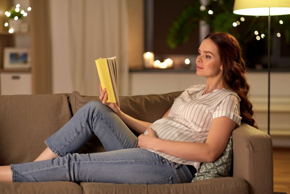 pregnancy and people concept - happy smiling pregnant woman reading book on sofa at home. happy smiling pregnant woman reading book at home