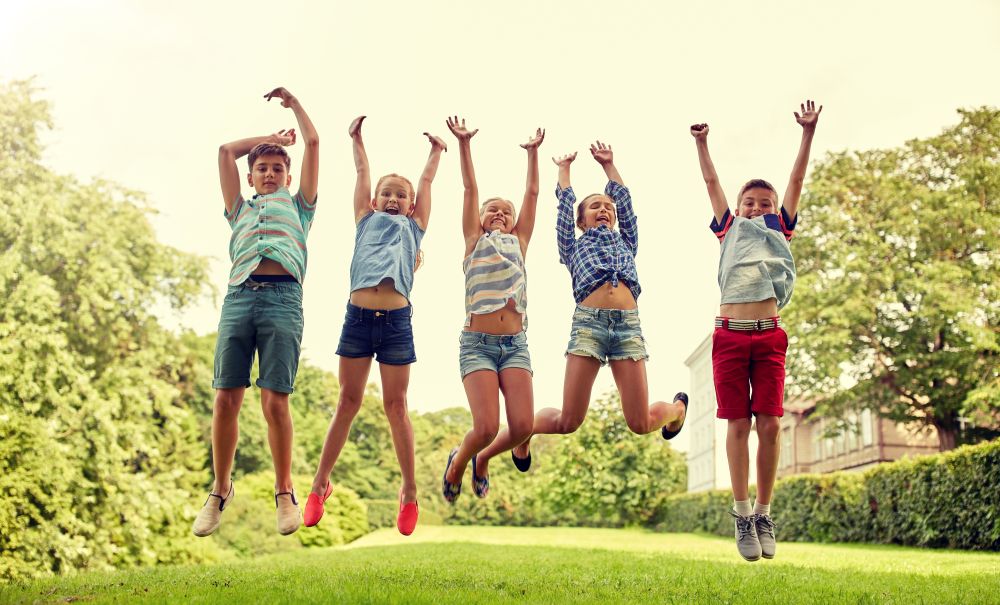 friendship, childhood, leisure and people concept - group of happy kids or friends jumping up and having fun in summer park. happy kids jumping and having fun in summer park