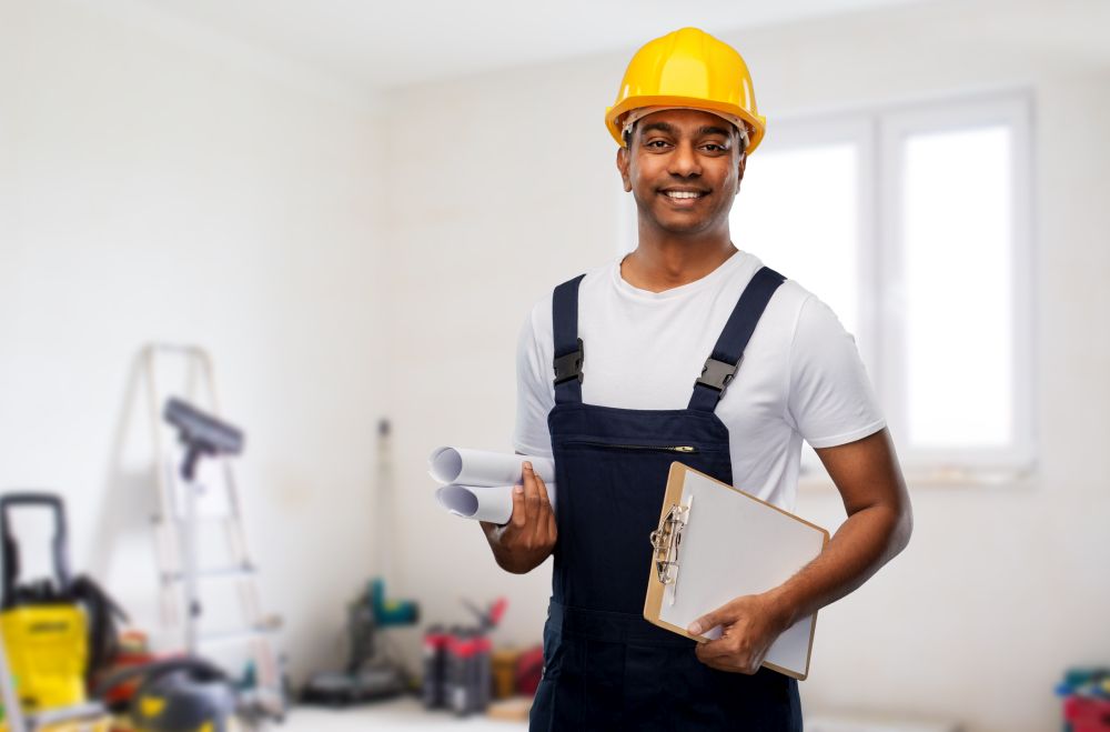profession, construction and building - happy smiling indian builder in helmet with blueprint and clipboard over home or apartment room background. happy indian builder with blueprint and clipboard