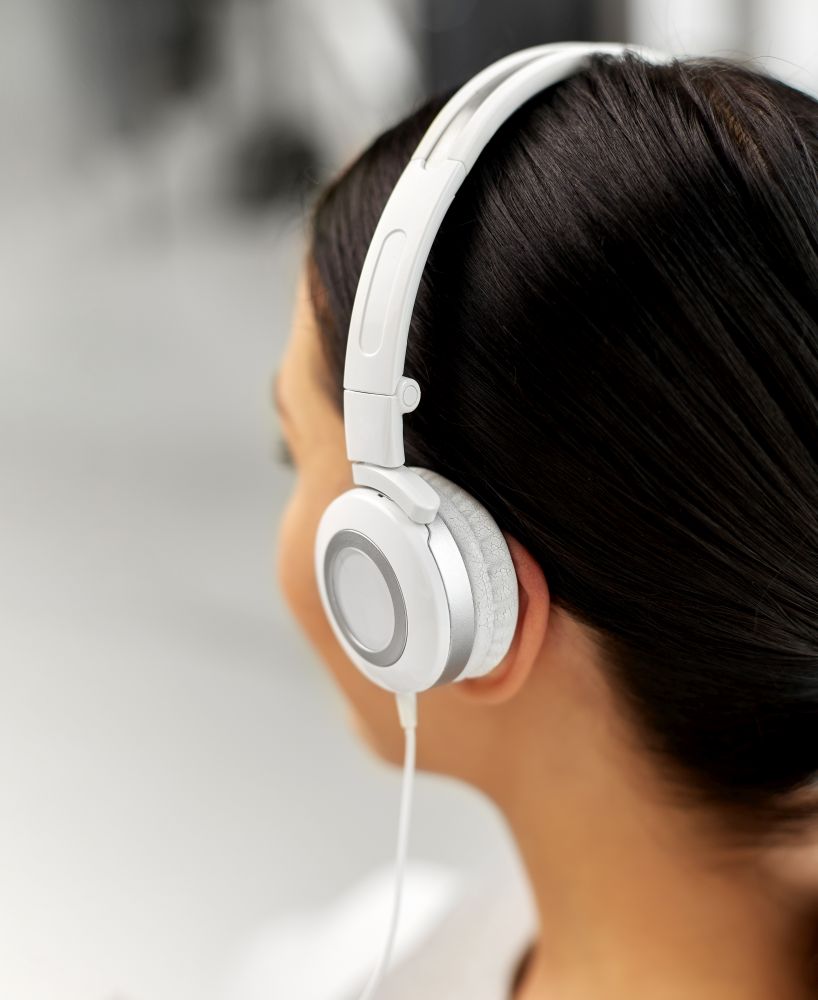 people, technology and audio equipment concept - close up of woman in headphones listening to music. close up of woman in headphones listening to music