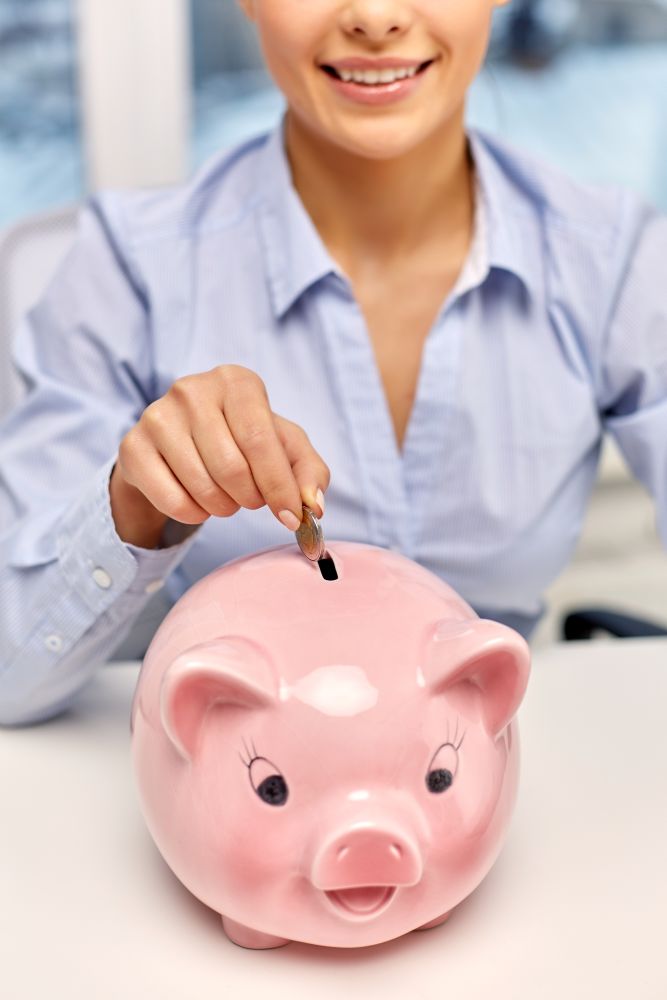 business, finances and investment concept - close up of happy smiling businesswoman with piggy bank and coin at office. businesswoman with piggy bank and coin at office