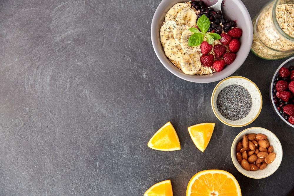 food and breakfast concept - oatmeal cereals in bowl with wild berries, fruits, almond nuts and poppy seeds on slate stone table. cereal with berries, fruits, nuts and poppy seeds