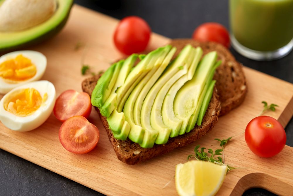 food, eating and breakfast concept - toast bread with sliced avocado, eggs and cherry tomatoes on wooden cutting board. toast bread with avocado, eggs and cherry tomatoes